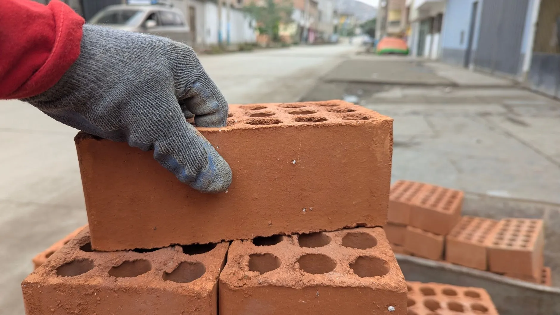 A gloved hand setting a clay brick onto a stack on site