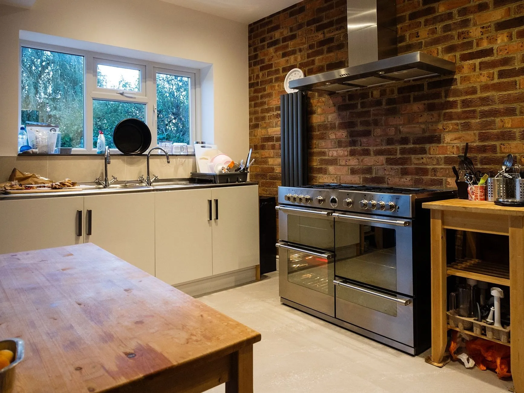 A kitchen with an exposed brick wall, a stainless range cooker and a wooden table where a dividing wall used to stand