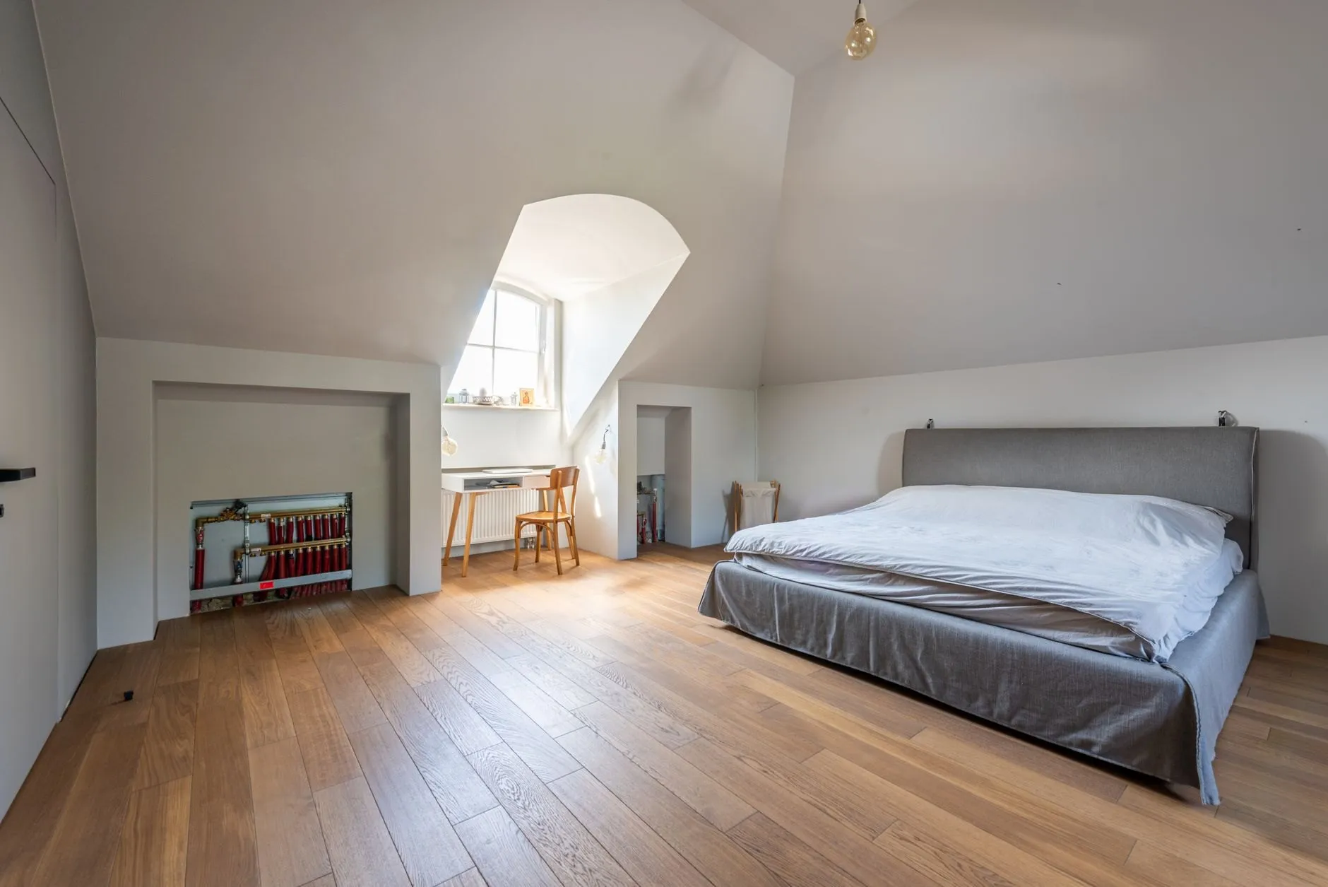A finished loft bedroom with a dormer window, oak floor and a double bed under the sloping ceiling