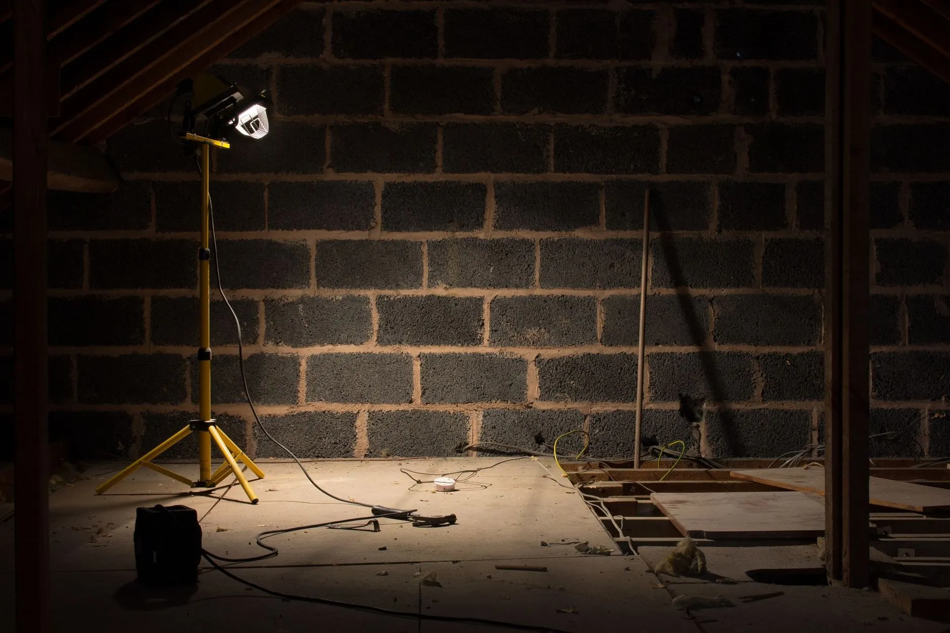 A loft mid-conversion with a bare blockwork gable and a site work light standing on a tripod